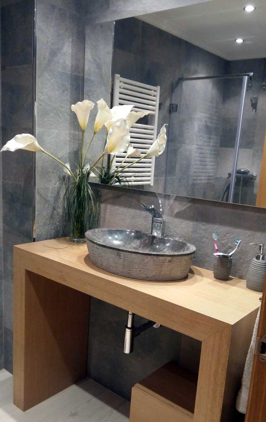 Baño con tocador de madera, lavabo de piedra, flores y un gran espejo.