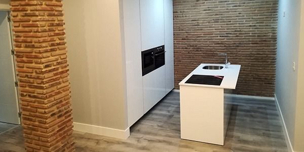 Cocina moderna con gabinetes blancos, isla, pared de ladrillo a la vista y columna de ladrillo.