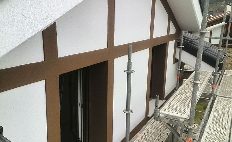 Exterior de un edificio con paredes blancas, vigas marrones y andamios.