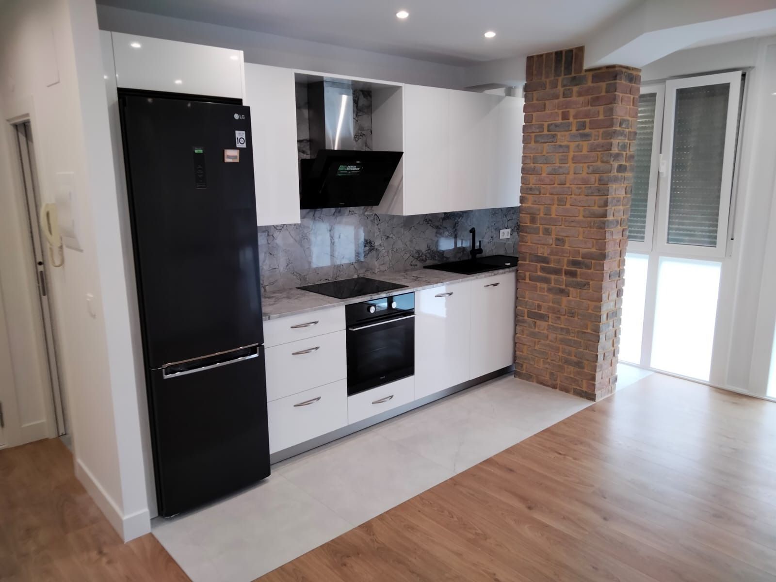 Cocina moderna con gabinetes blancos, electrodomésticos negros, encimeras de granito y pared con acento de ladrillo.