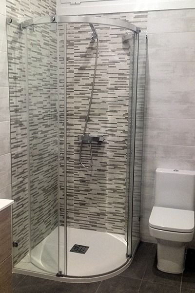 Cabina de ducha con puertas de cristal y WC en un baño con paredes alicatadas.
