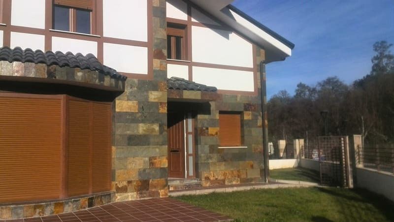 Casa de piedra y madera con césped y árboles al fondo bajo un cielo azul.