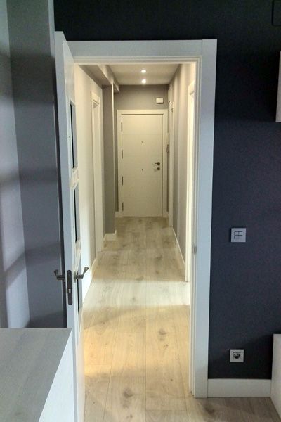 Un pasillo con suelo de madera y puertas blancas. Las paredes son de color gris oscuro y los marcos de las puertas son blancos.