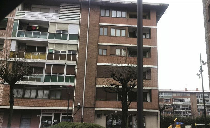 Edificios de apartamentos de ladrillo con balcones, árboles y cielo nublado.