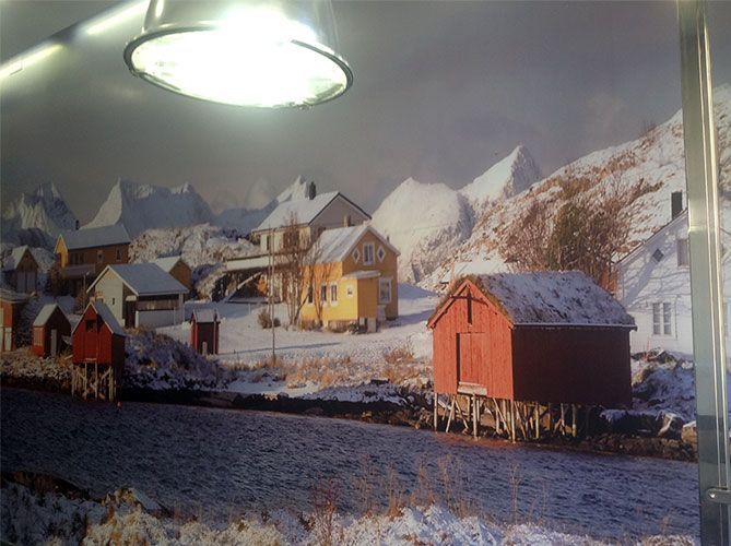 Escena de pueblo nevado con edificios rojos y amarillos, montañas al fondo.