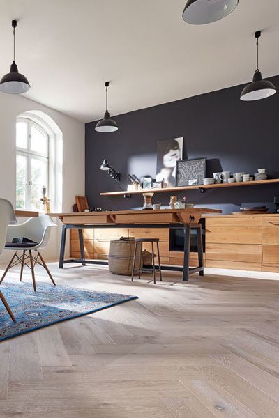 Cocina con isla de madera, gabinetes y piso de espiga, pared decorativa negra y luces colgantes.