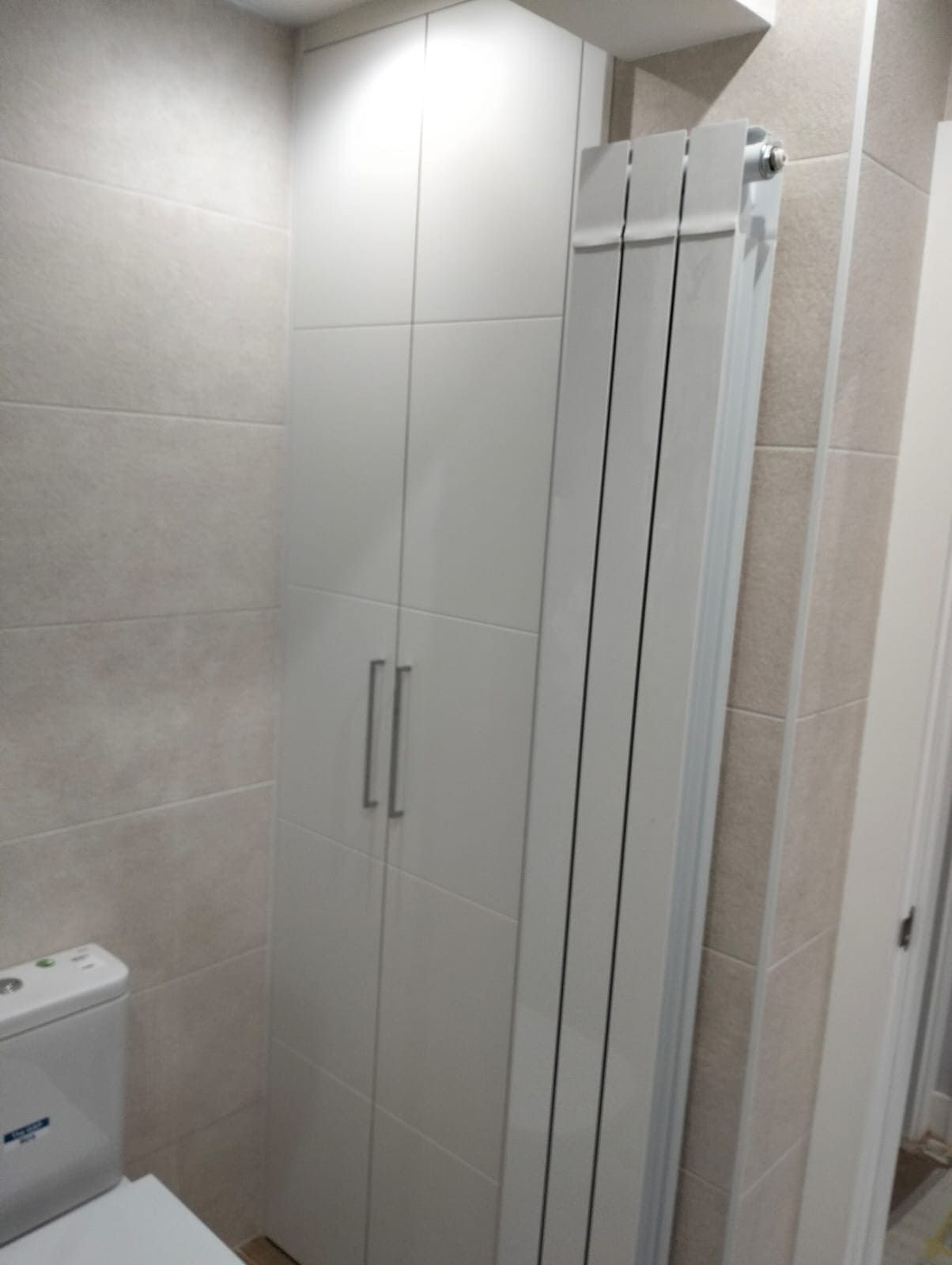 Baño con mueble blanco, radiador y sanitario contra paredes alicatadas.