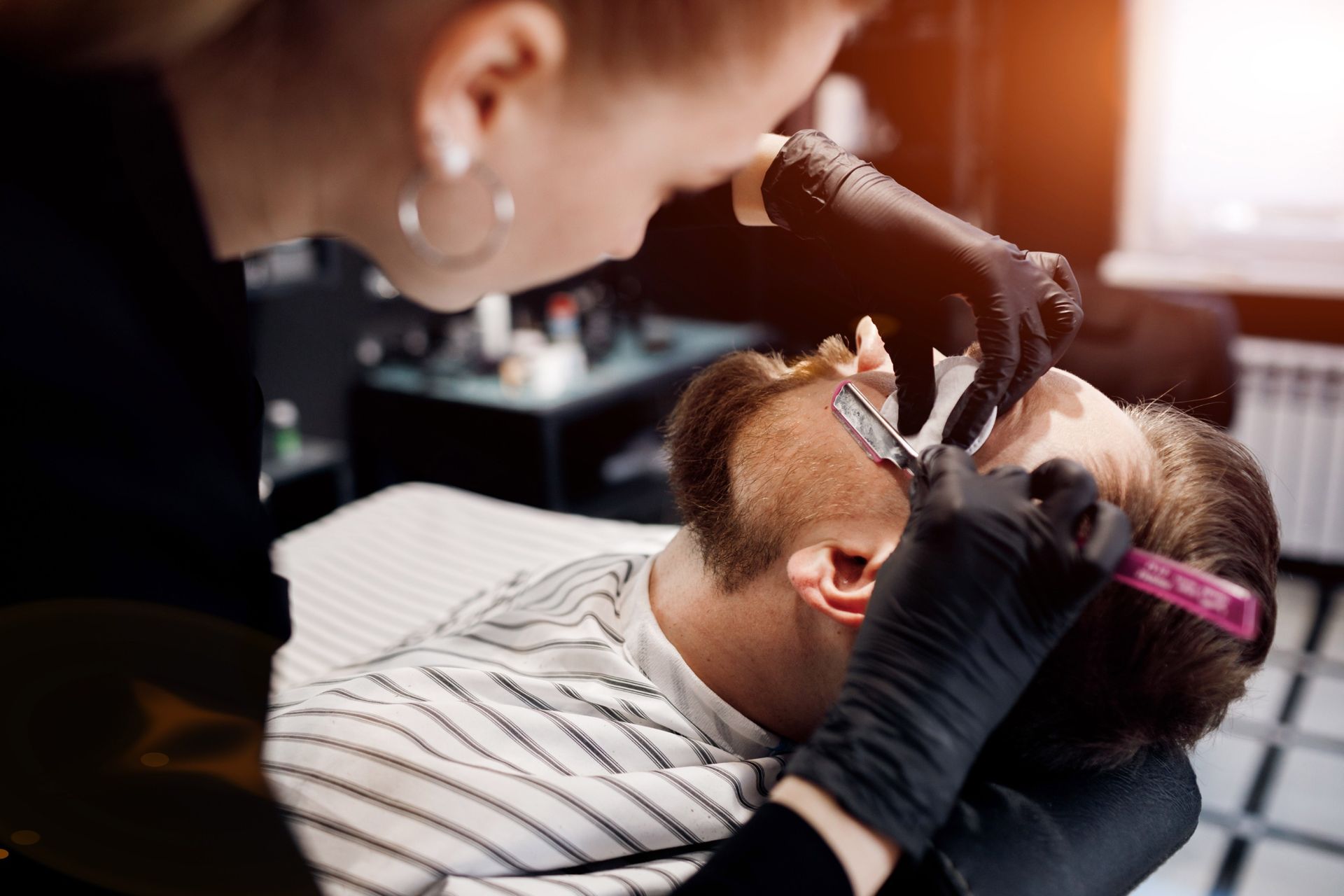 Una mujer está afeitando la barba de un hombre con una navaja en una barbería.