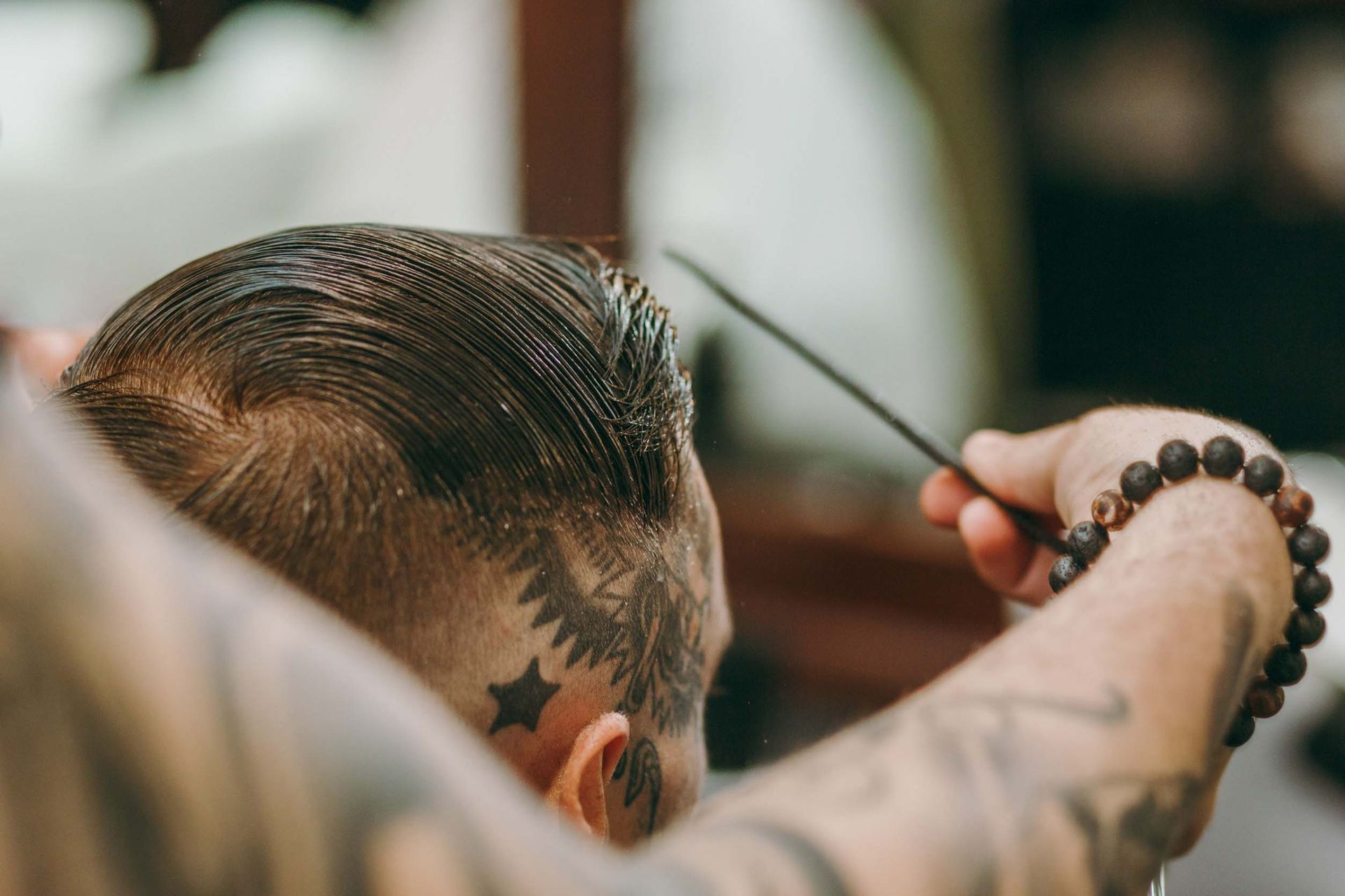 Un hombre con tatuajes en la cara se está cortando el pelo en un barbero.
