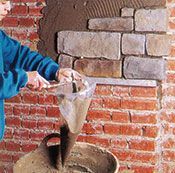 Una persona está vertiendo cemento en un cubo al lado de una pared de ladrillos.