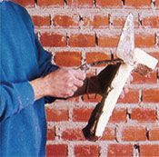 Un hombre sostiene un trozo de madera frente a una pared de ladrillos.