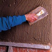 Una persona está aplicando adhesivo a una pared de ladrillos con una paleta.