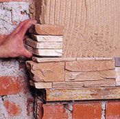 Una persona está instalando baldosas de piedra en una pared de ladrillos.