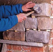 Un hombre está colocando ladrillos en una pared con un martillo.