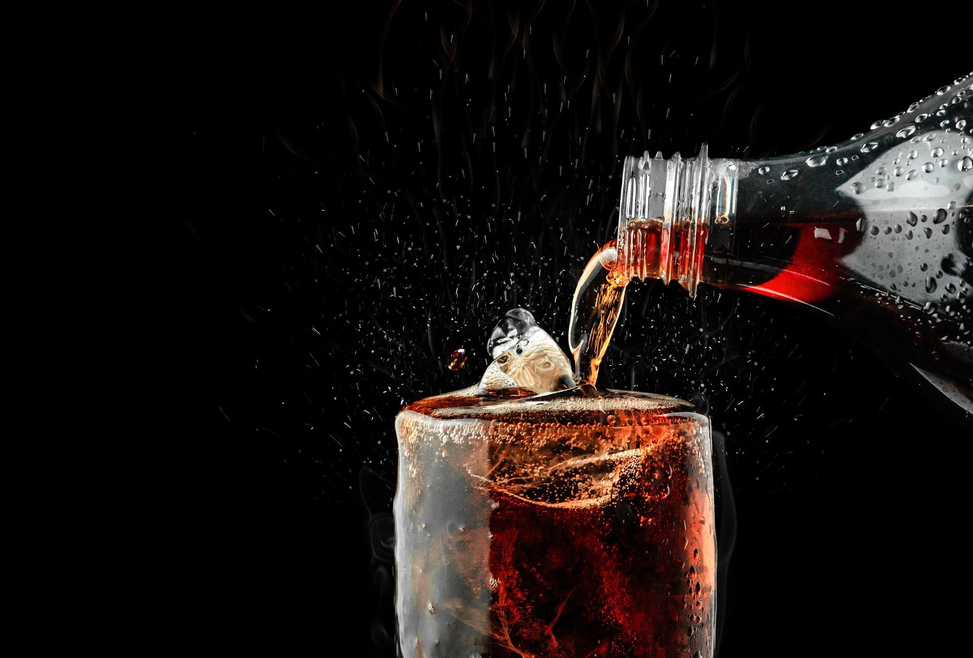 Du soda est versé depuis une bouteille dans un verre contenant des glaçons.