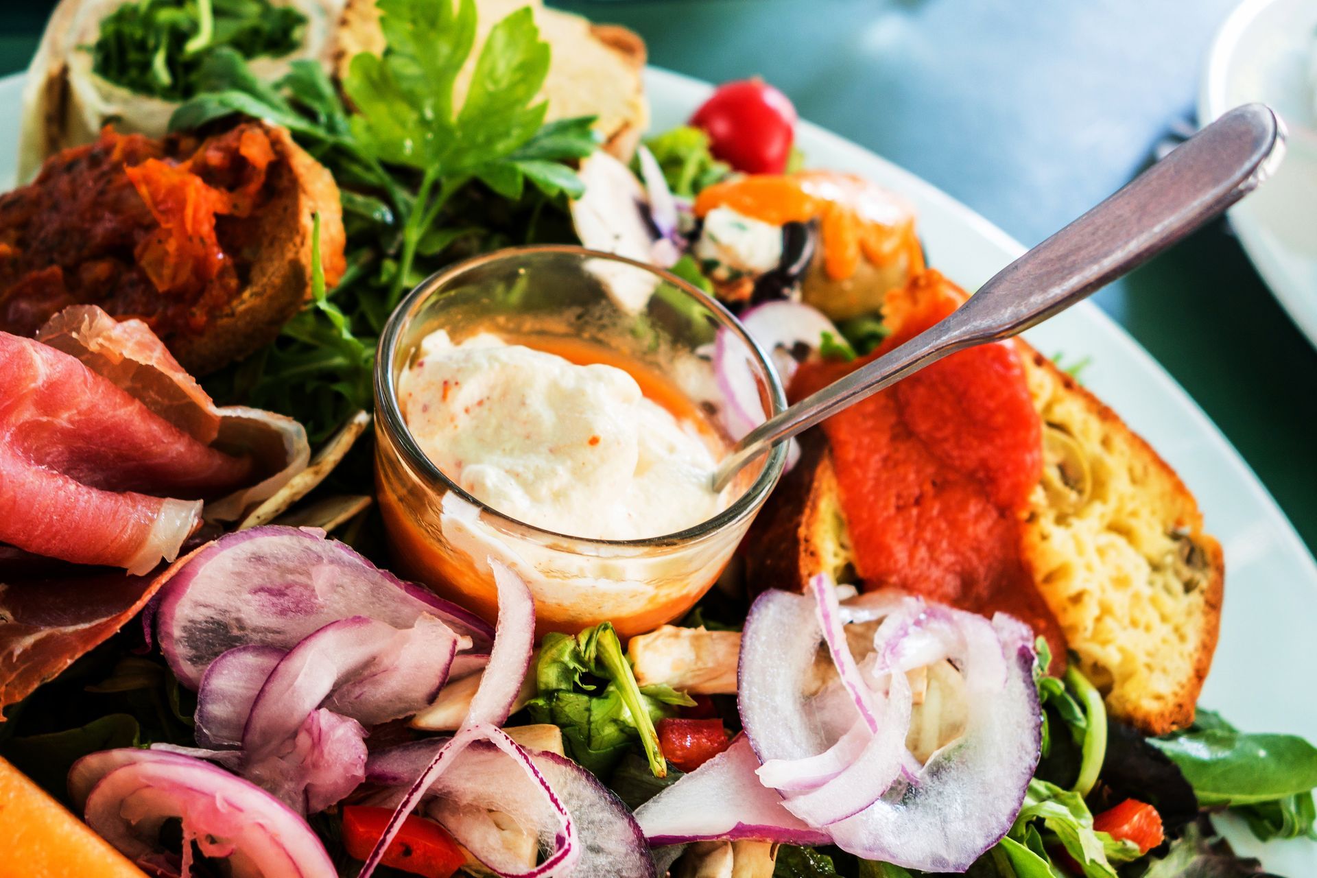 Salade composée avec légumes, saumon et sauce crémeuse, servie dans un saladier avec une cuillère.