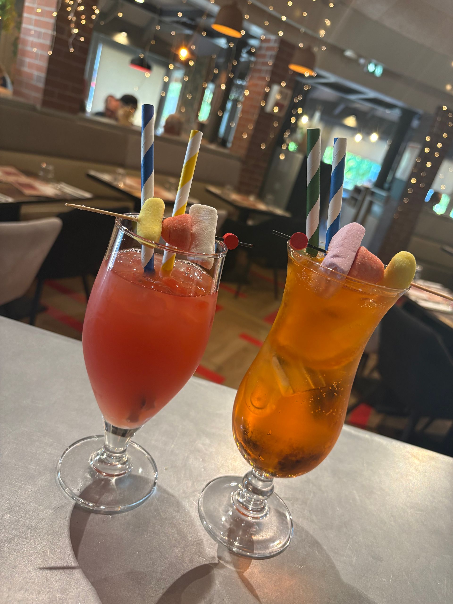 Deux cocktails avec pailles et garnitures de fruits sur une table dans un restaurant.