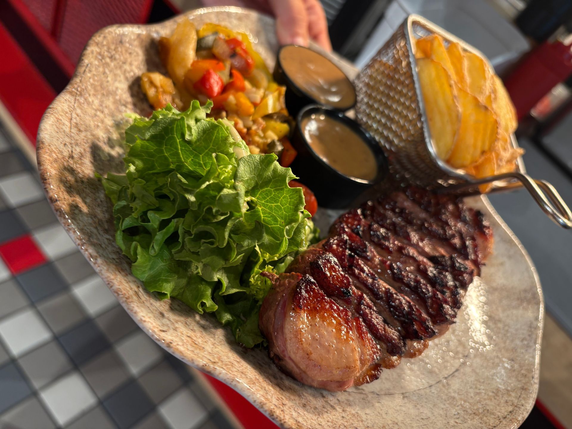 Steak grillé avec salade, légumes et sauces, servi dans une assiette rustique.