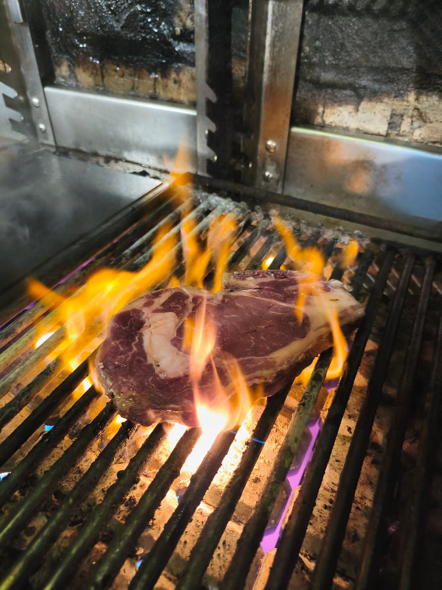 Un steak grésille sur un gril avec de hautes flammes dans un poste de cuisson.