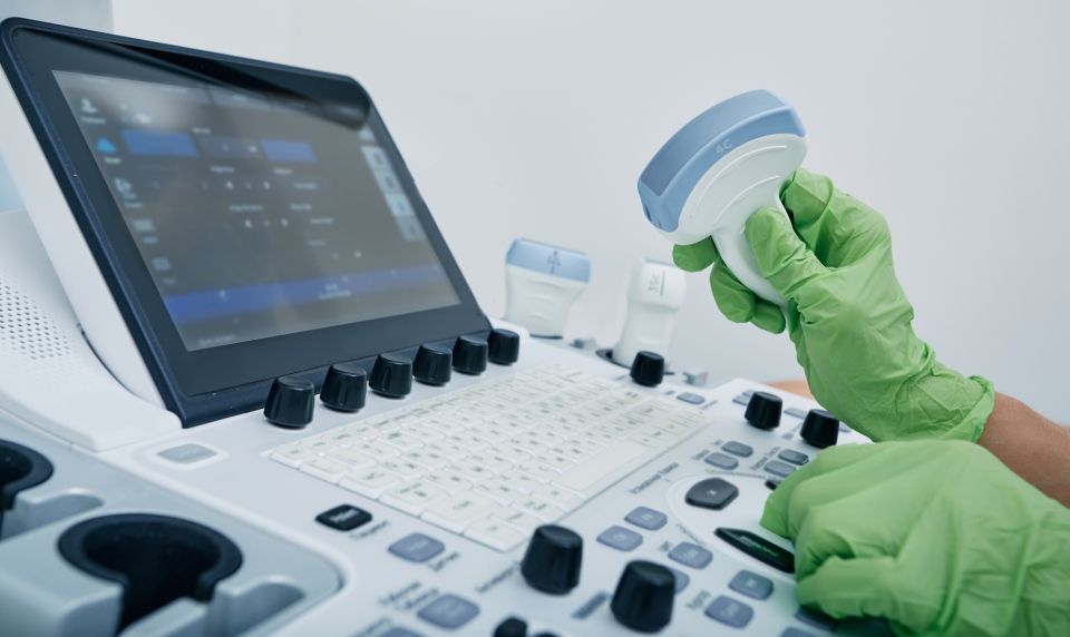 Eine Person mit grünen Handschuhen benutzt ein Ultraschallgerät.