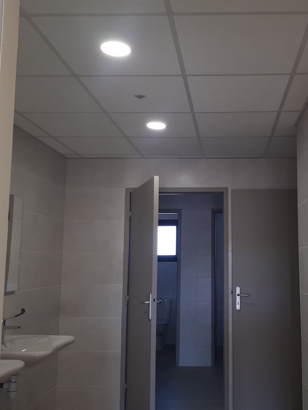 Toilettes publiques avec murs gris, portes ouvertes et plafonniers