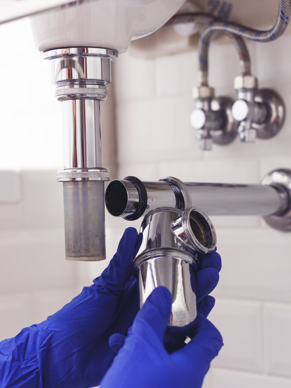 Des mains gantées de bleu assemblent un siphon d'évier chromé