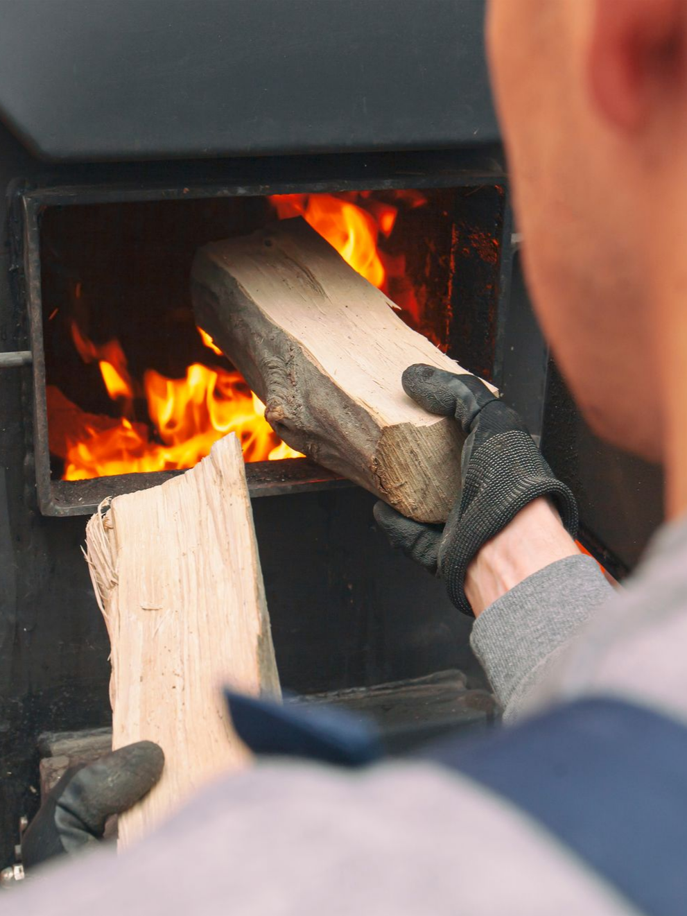 Une personne portant des gants place du bois dans un poêle à bois en feu