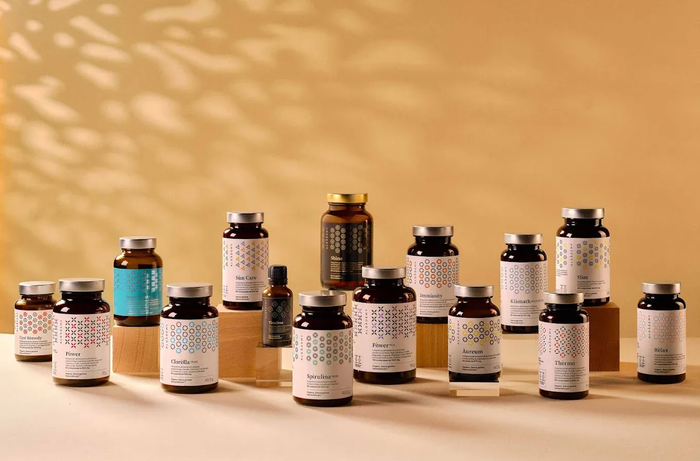 Raccolta di flaconi di integratori Algademy di varie dimensioni, disposti su blocchi di legno su uno sfondo marrone chiaro.