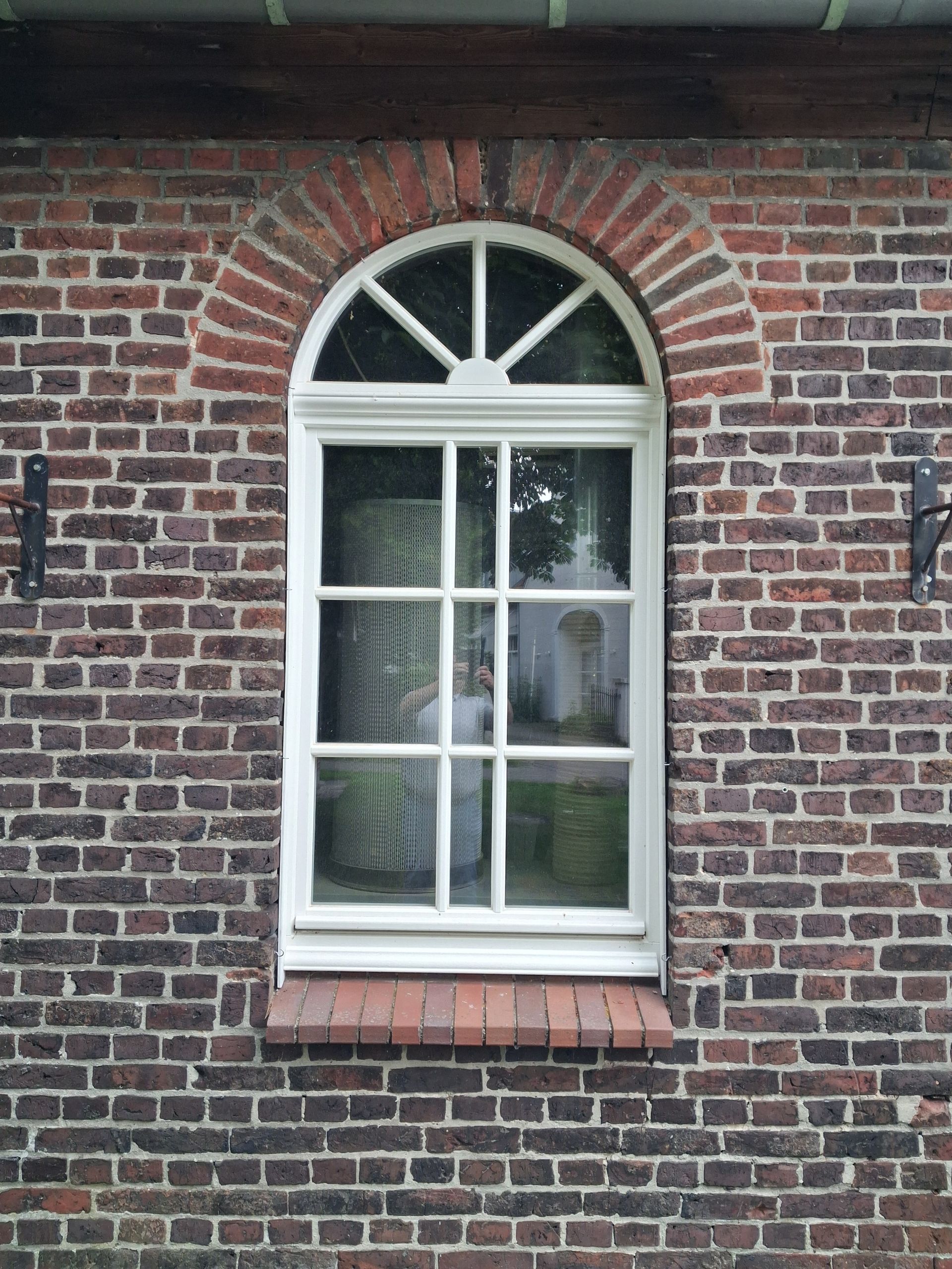 Weißes Rundbogen-Sprossenfenster in Ziegelwand.