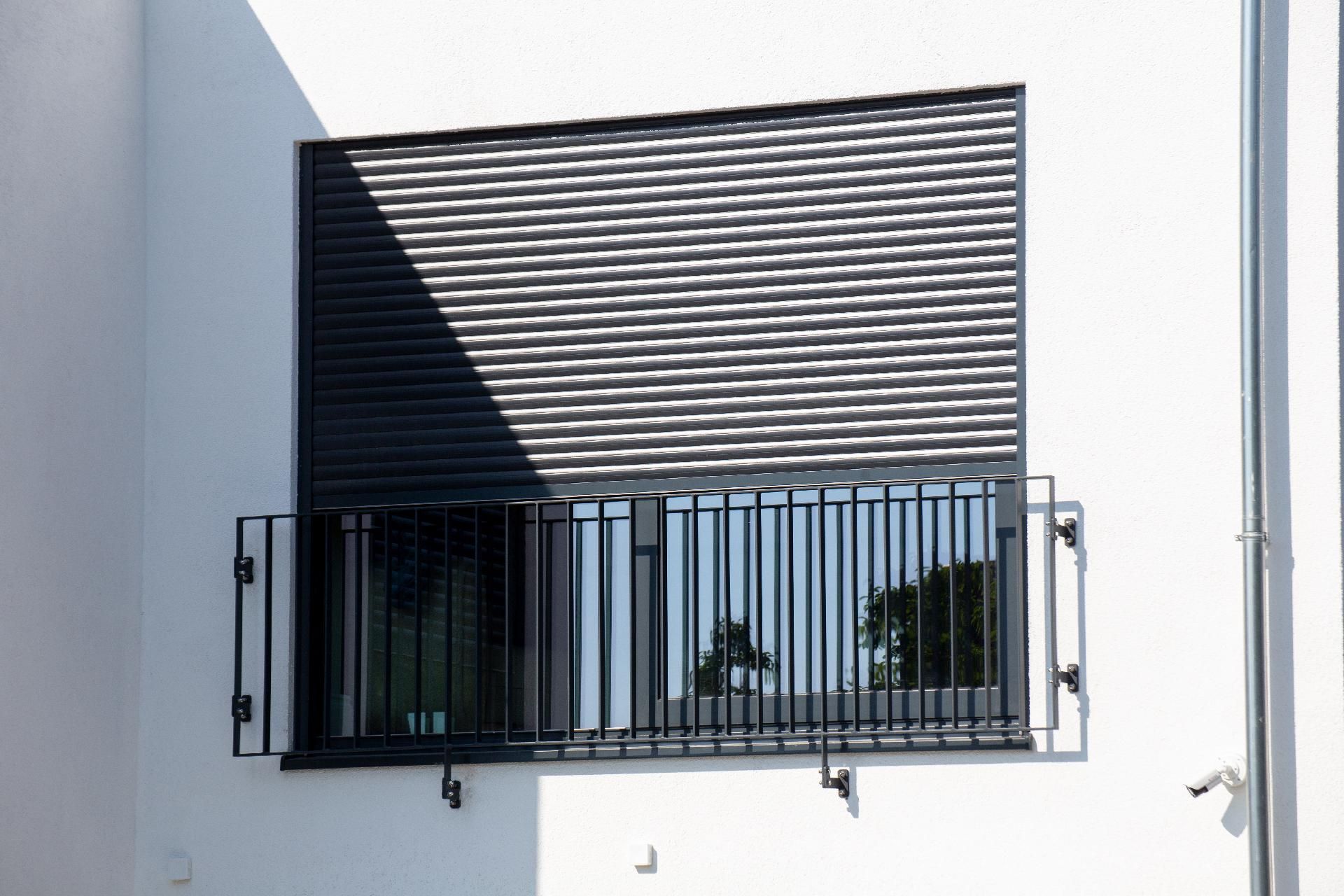 Fenster mit modernem dunklem Rollladen und schwarzem Geländer.