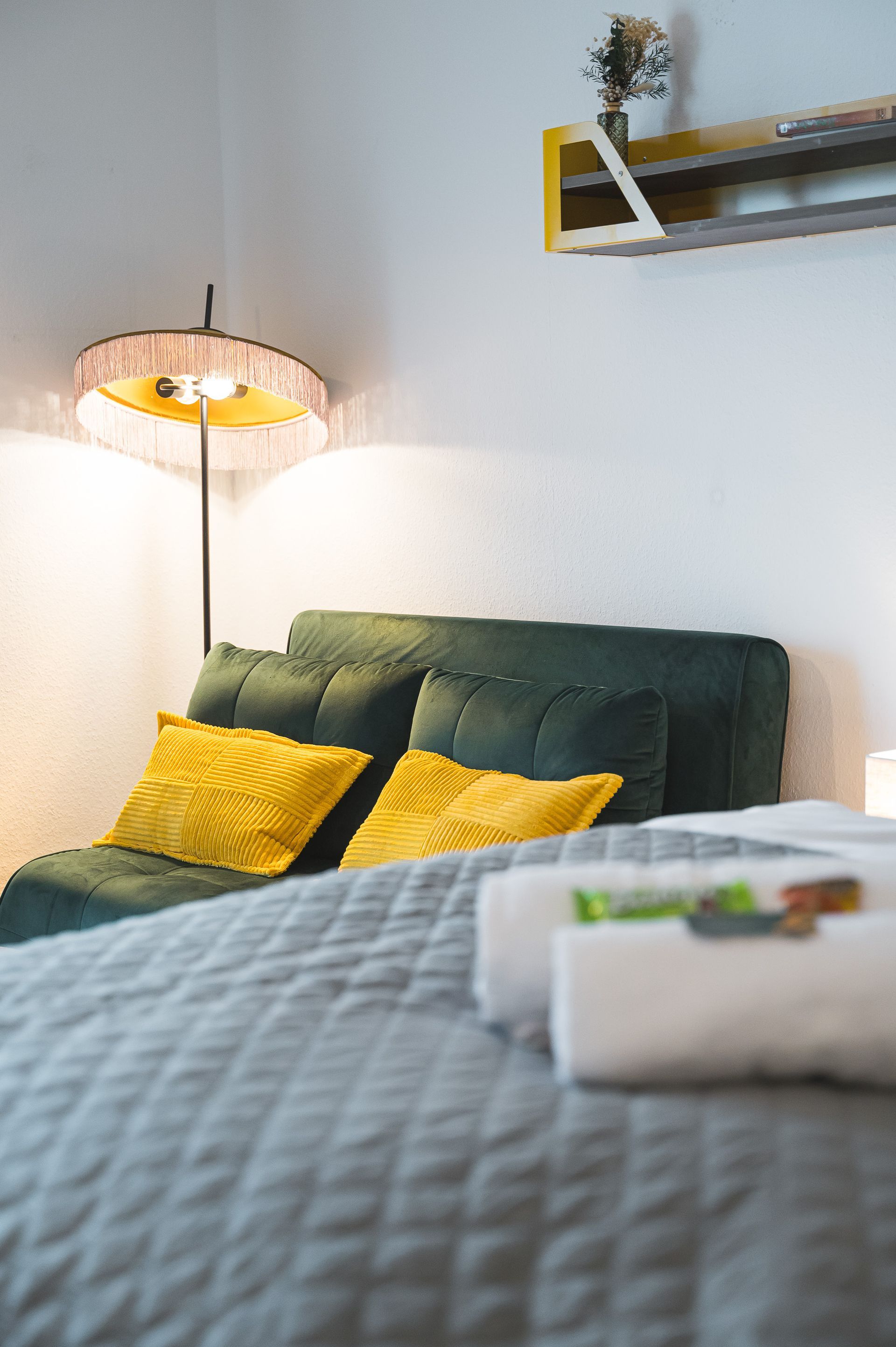 Bedroom with green headboard, yellow pillows, grey bedspread, and a floor lamp.