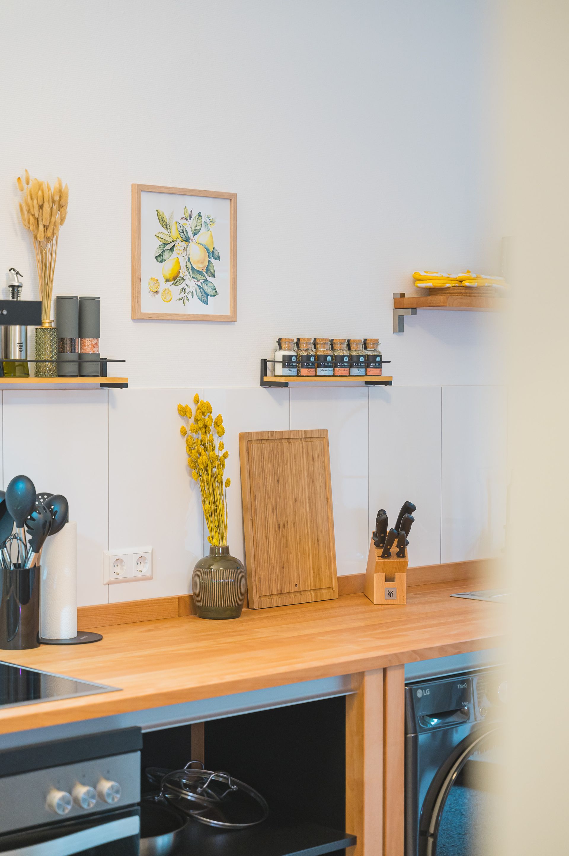Kitchen with wooden countertops, shelves holding spices, a framed picture, and a vase of yellow flowers.