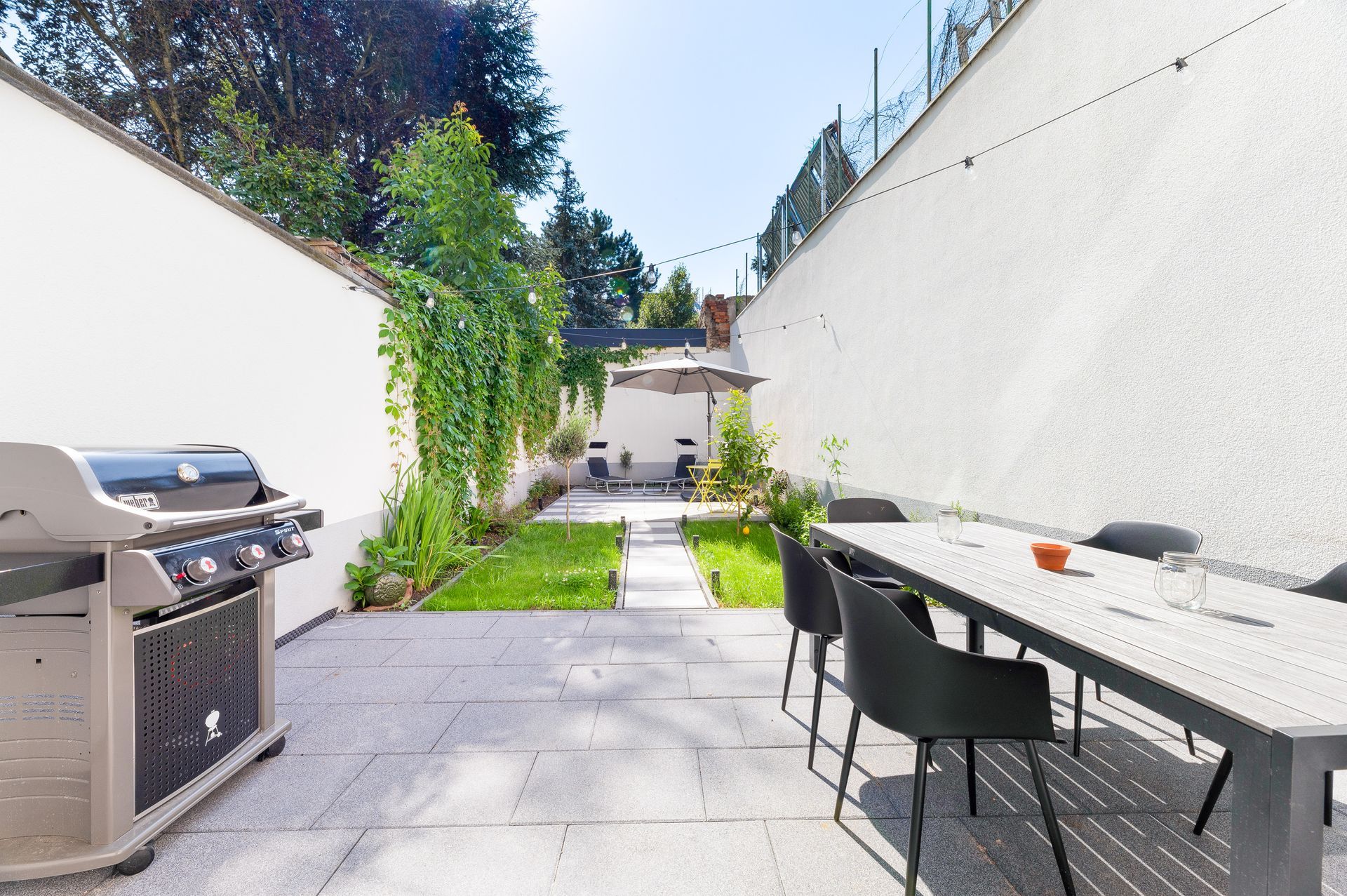 Backyard patio with grill, dining table, small lawn, and white walls.