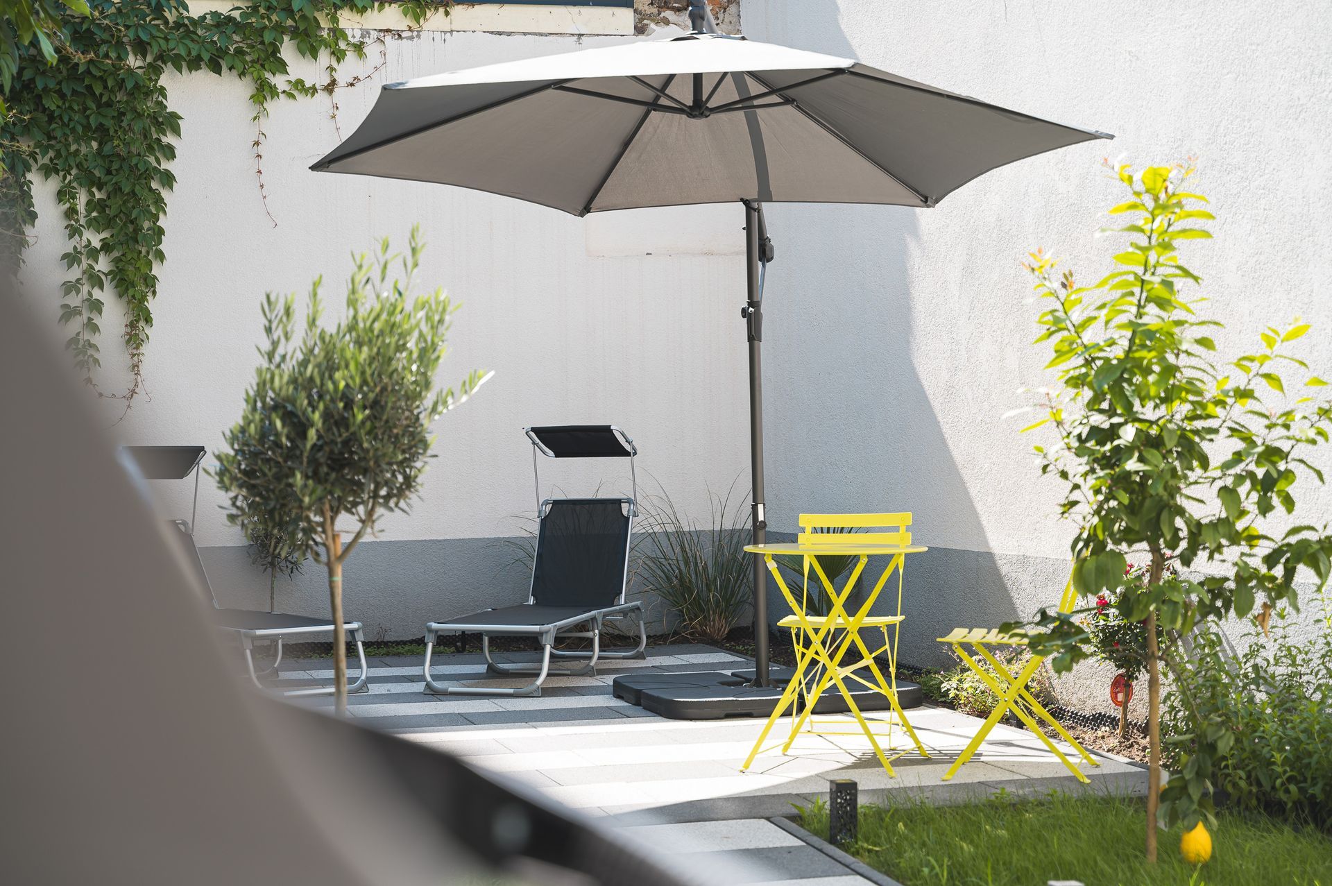 Patio with umbrella, yellow table and chairs, trees, and white wall.