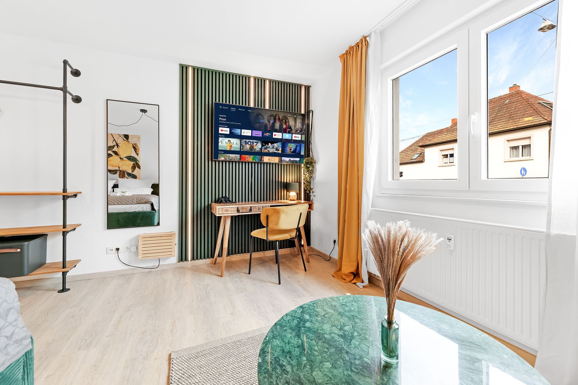 Brightly lit room with a TV, desk, window, and round marble coffee table.
