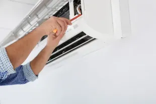 Un hombre está arreglando un aire acondicionado con un destornillador.