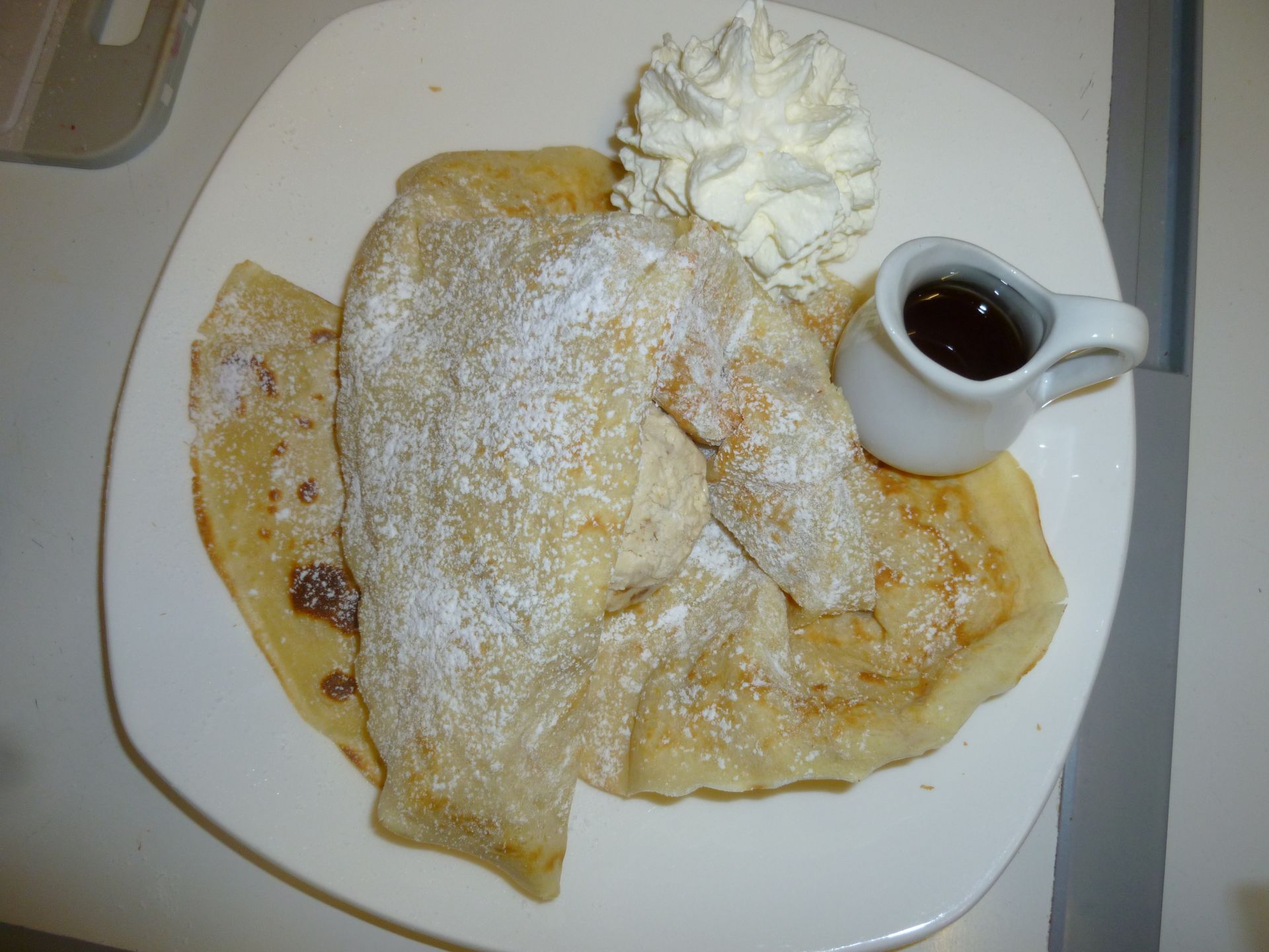 Ein Teller Pfannkuchen mit Schlagsahne und Sirup auf einem Tisch.