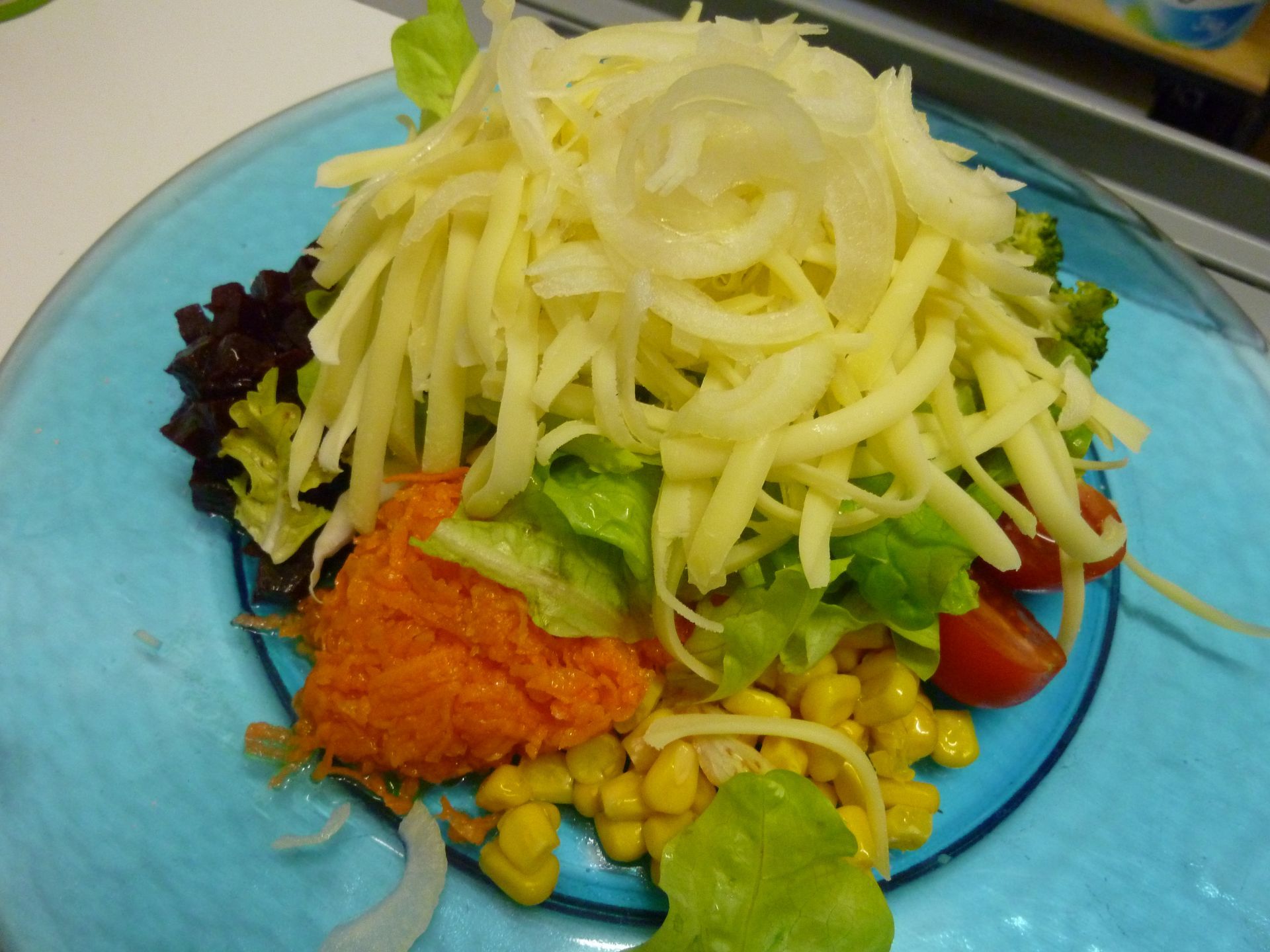 Ein Salat mit Karotten, Tomaten, Mais und Käse auf einem blauen Teller