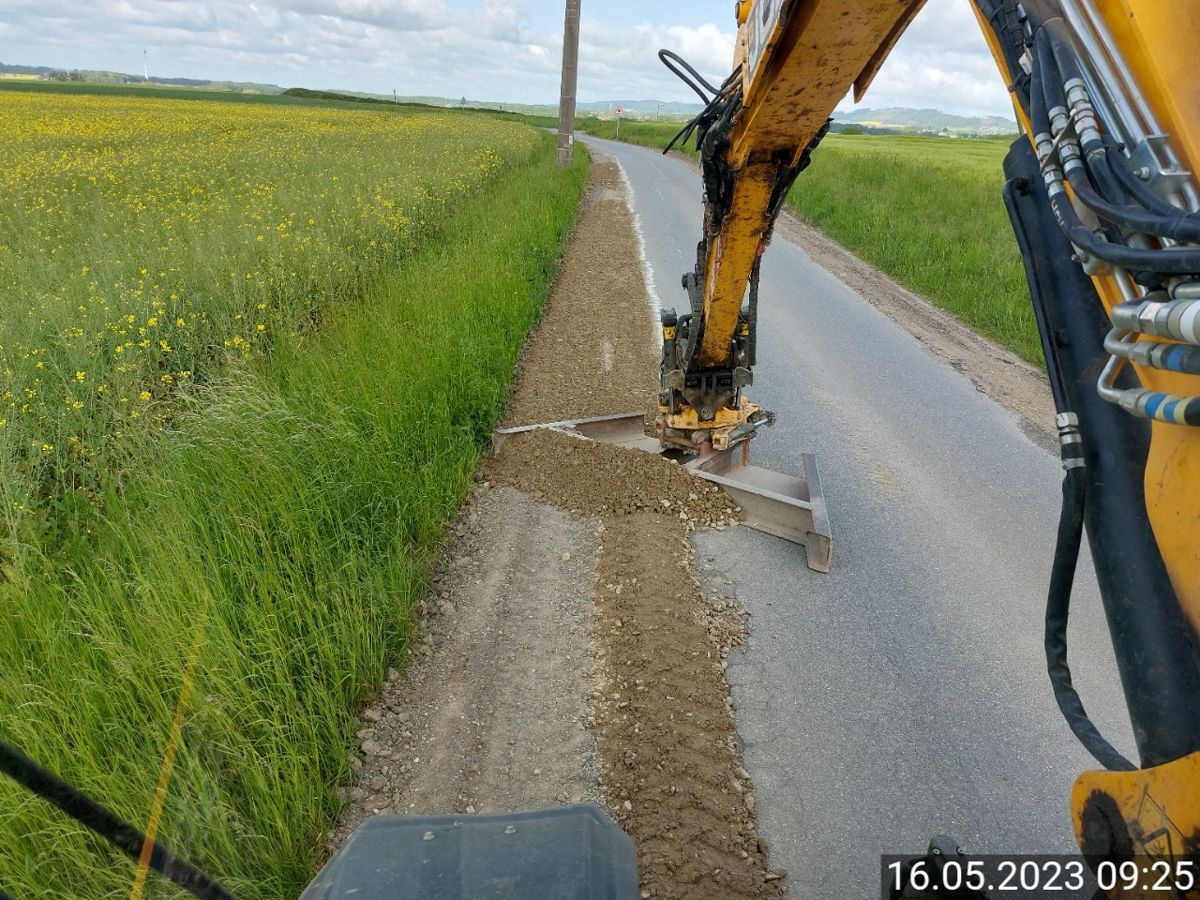 Ein gelber Bagger gräbt mitten auf einer Straße ein Loch.