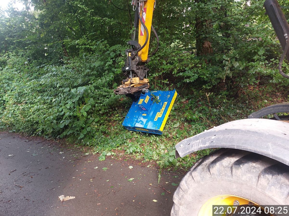 Ein Traktor schneidet Gras am Straßenrand.