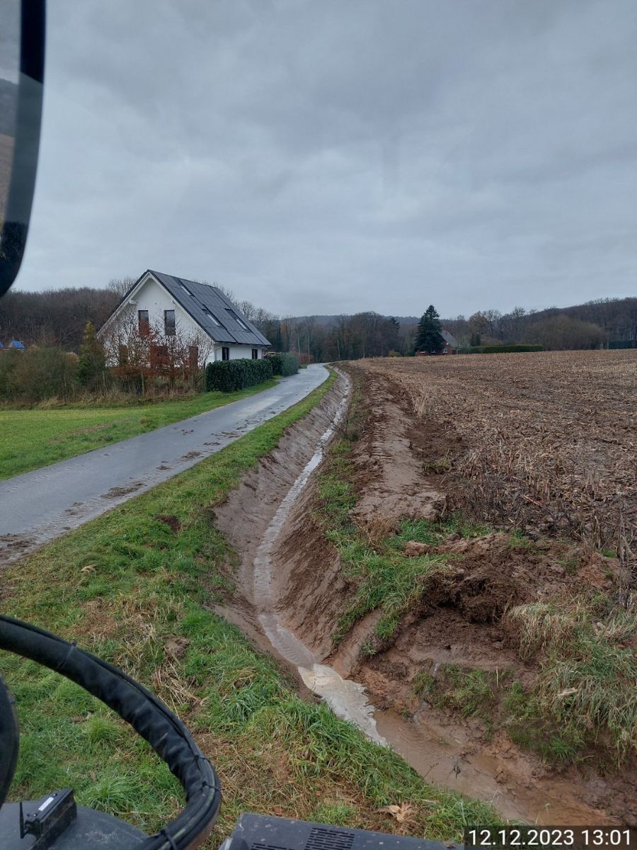 Ein Traktor fährt auf einer schlammigen Straße neben einem Haus entlang.