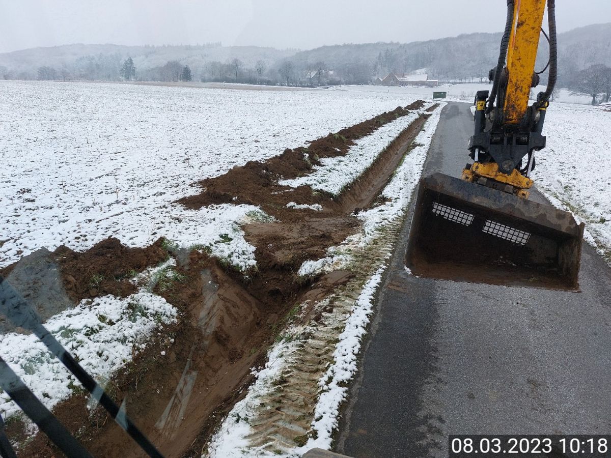 Ein gelber Bagger gräbt einen Graben in den Schnee.