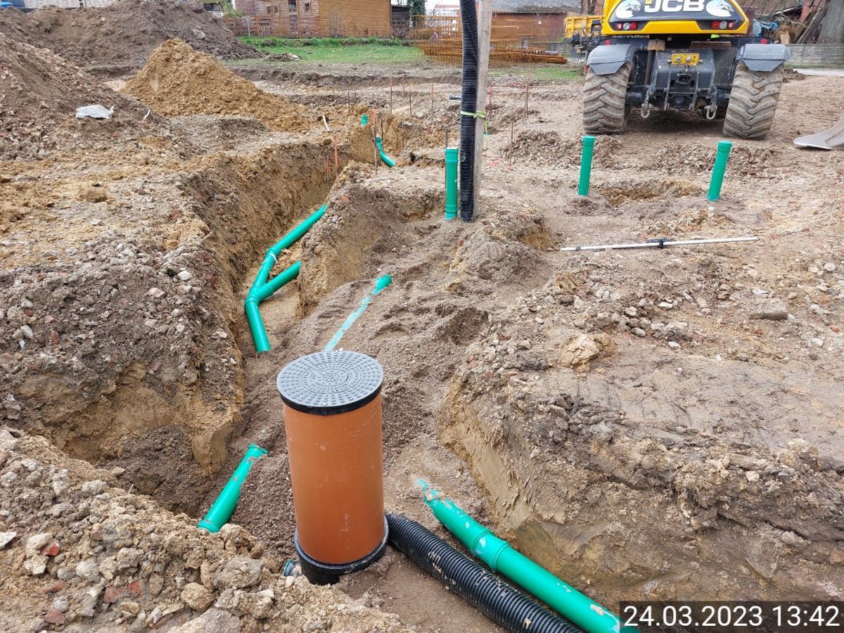 Eine Baustelle mit einem Traktor im Hintergrund und einem Haufen Rohre im Dreck.