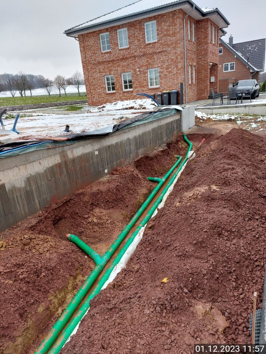 Ein Backsteinhaus, vor dem grüne Rohre aus dem Boden kommen.