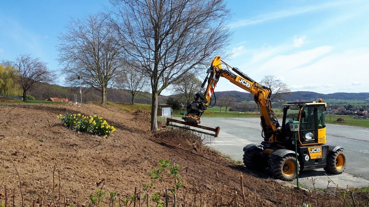 Ein gelber Bagger fällt auf einem Feld einen Baum.