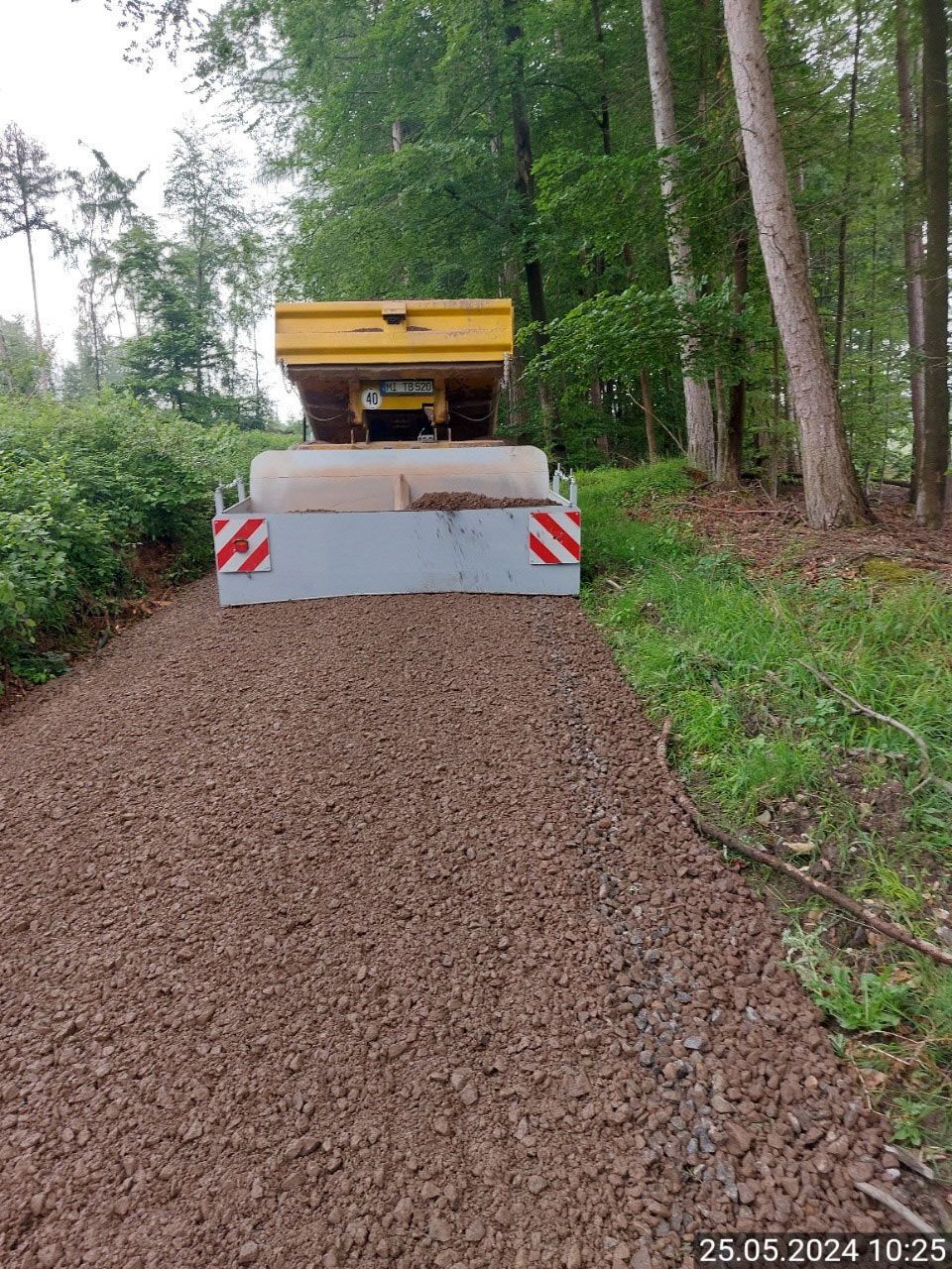 Ein gelber Lastwagen fährt auf einer Schotterstraße durch den Wald.