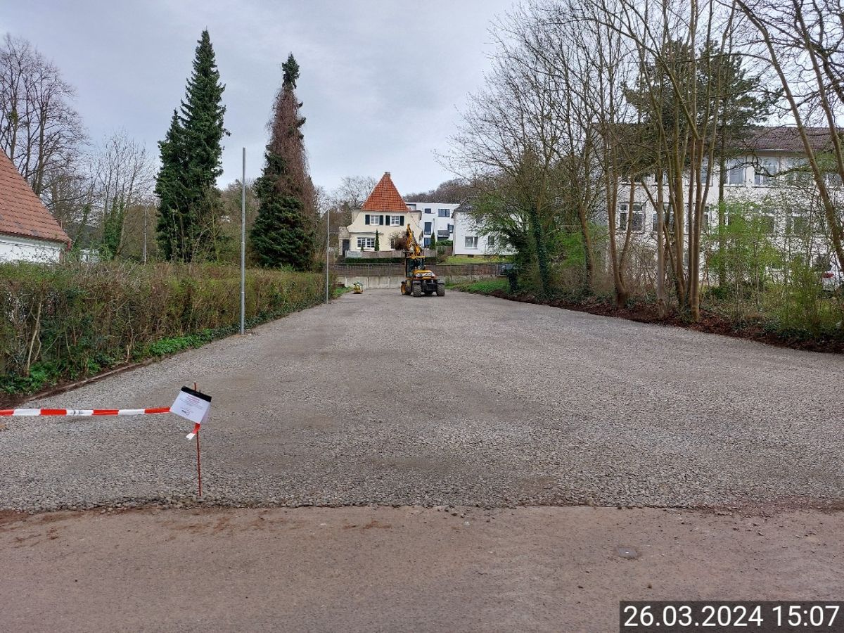 Eine Schotterstraße mit einem Zaun und einem Haus im Hintergrund.