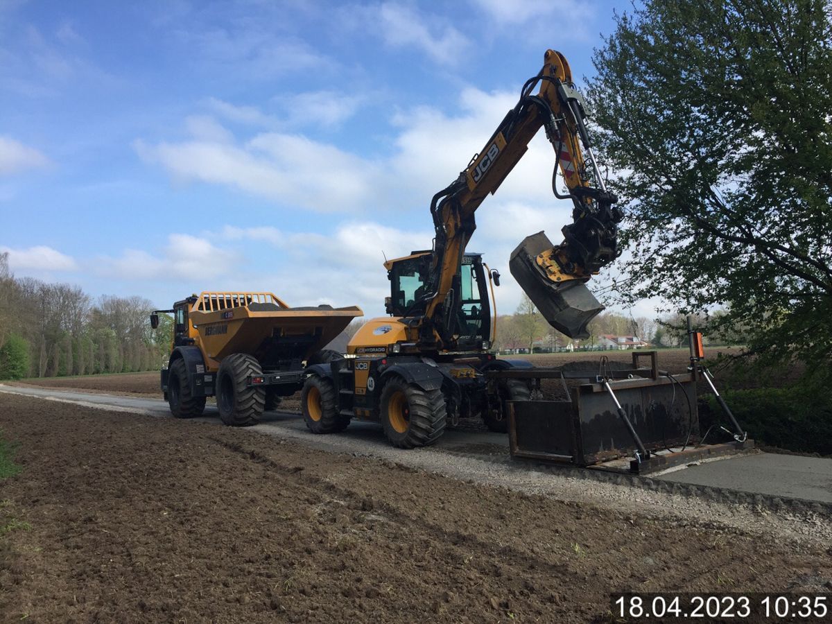 Ein Traktor fährt auf einer unbefestigten Straße neben einem Muldenkipper her.