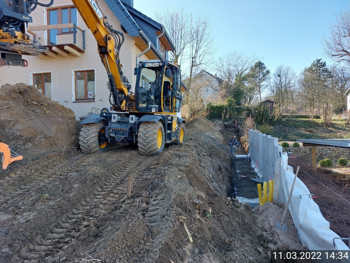 Ein gelber Bagger gräbt vor einem Haus ein Loch.