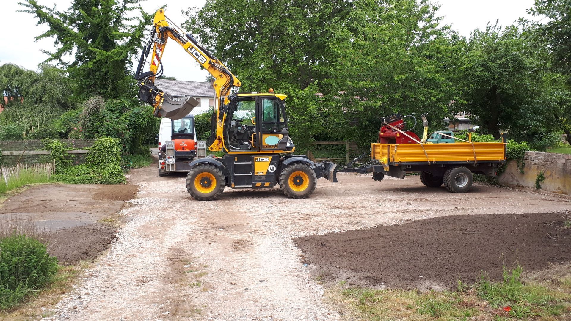 Ein gelber Bagger fährt neben einem gelben Muldenkipper auf einer unbefestigten Straße entlang.